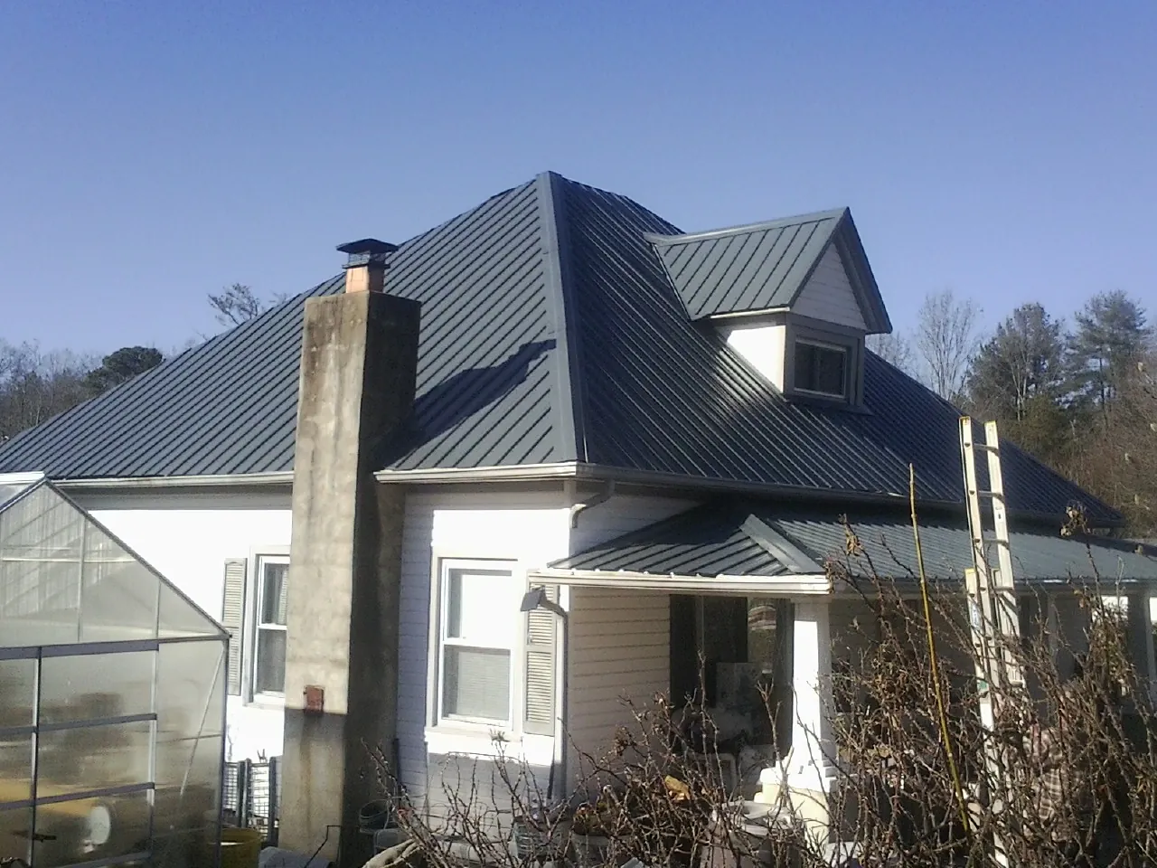 Dark blue standing seam metal roof on a white farmhouse with dormer in East Moriches