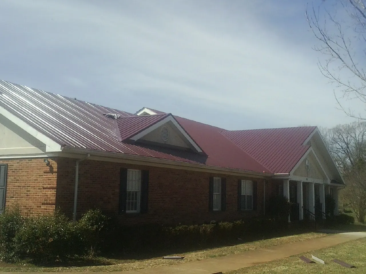 Red metal roof with gabled entries on a long brick building, from a Hail Damage Roof Repair job in East Moriches