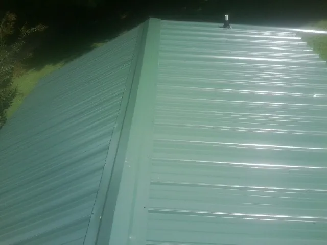 New green metal panels meeting at the ridge of a roof — Flat Roof Repair work by our crew in East Moriches