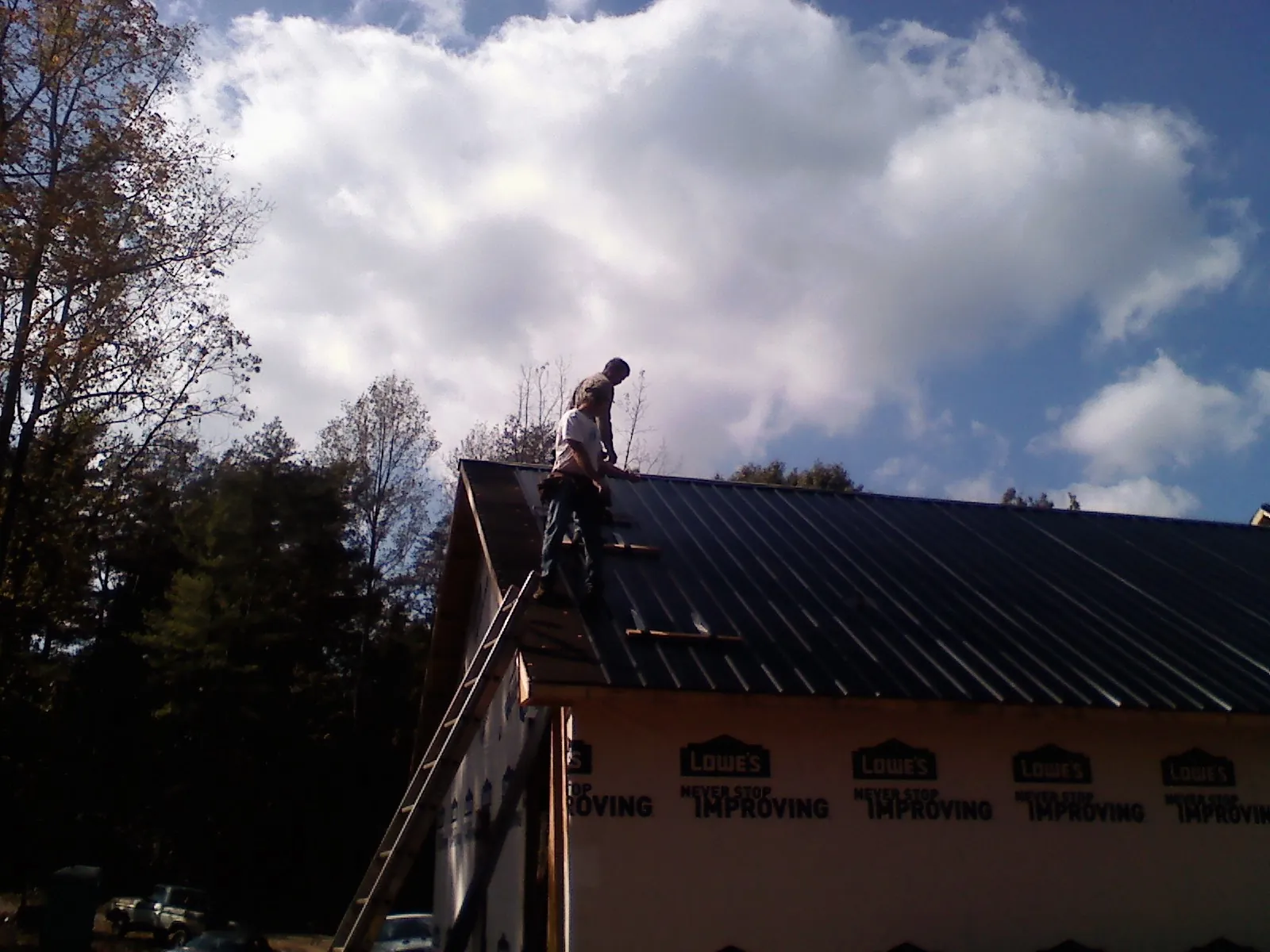Roofer fastening dark metal panels high against a cloudy sky, from a Roof Inspection job in East Moriches