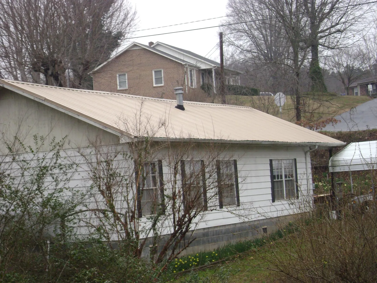Tan metal roof on a white sided house set into a hillside — Commercial Roofing by Roofing Brothers in East Moriches
