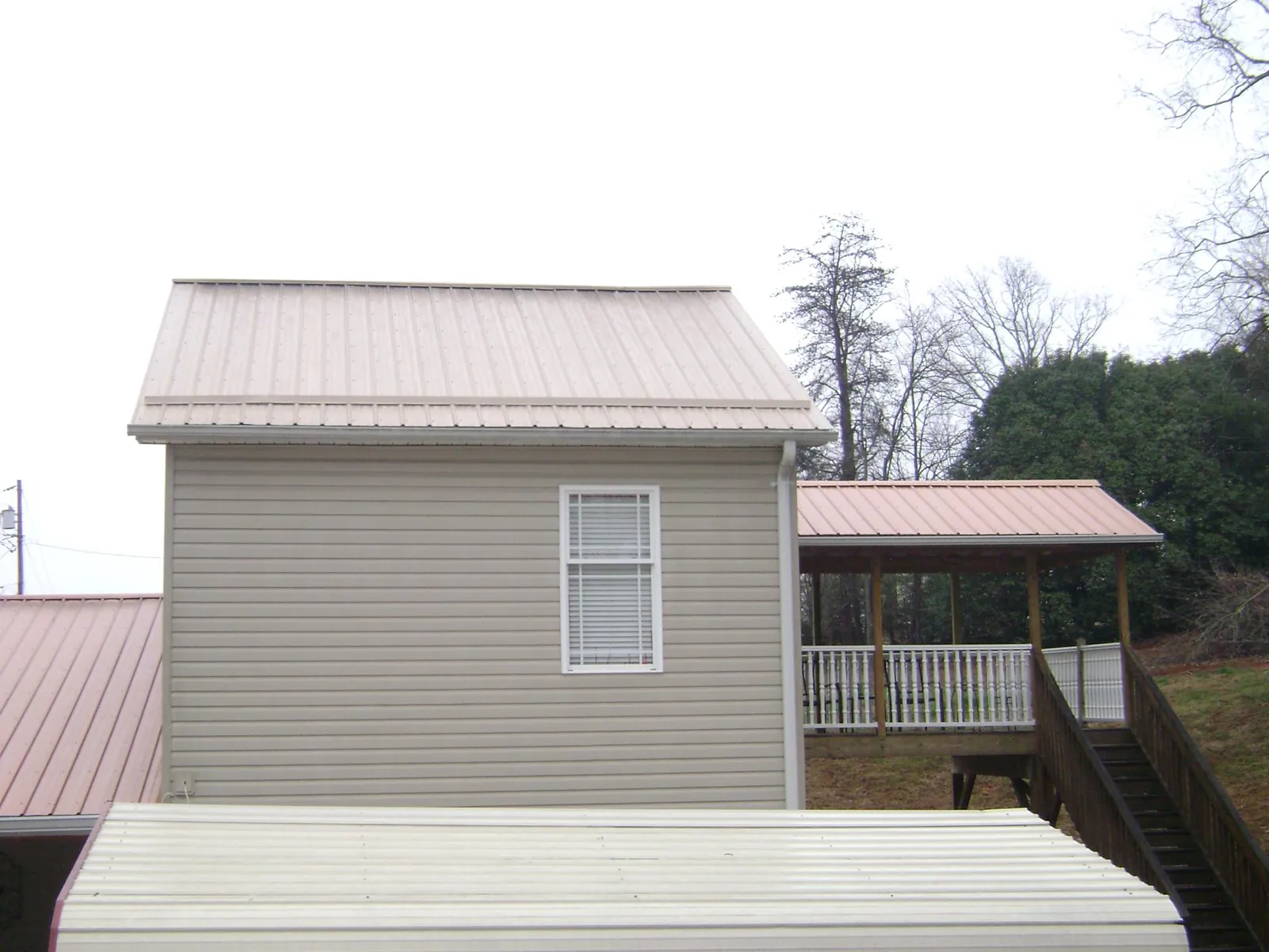 Tan metal roofs on a two story addition and attached porch, from a Roof Replacement job in East Moriches